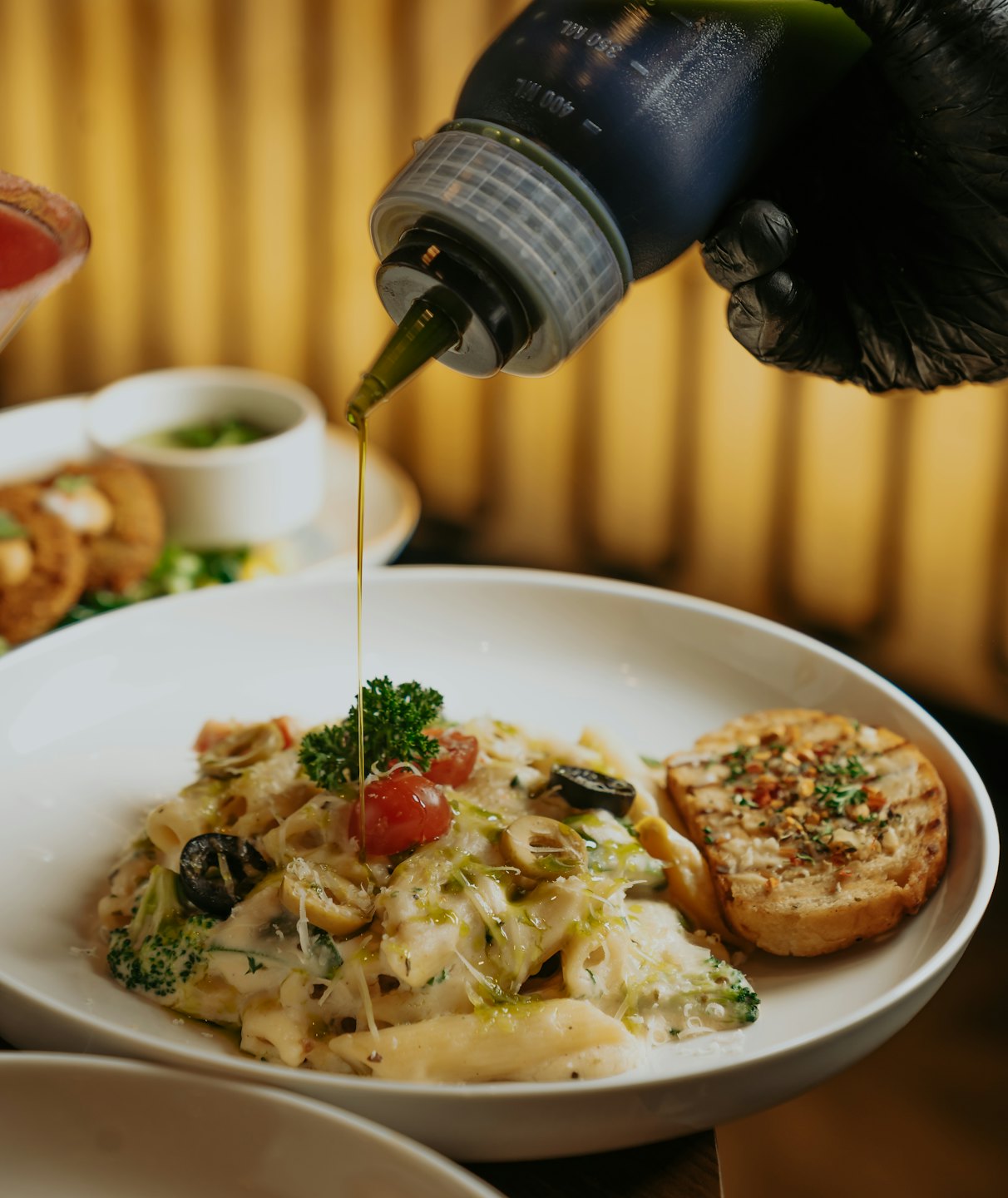 Una mano enguantada rocía aceite de oliva sobre un plato de pasta.