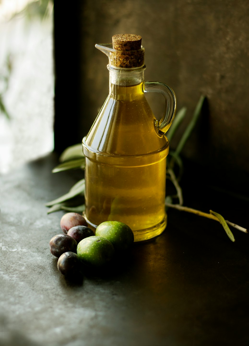 Botella de vidrio de aceite de oliva dorado con aceitunas y hojas.
