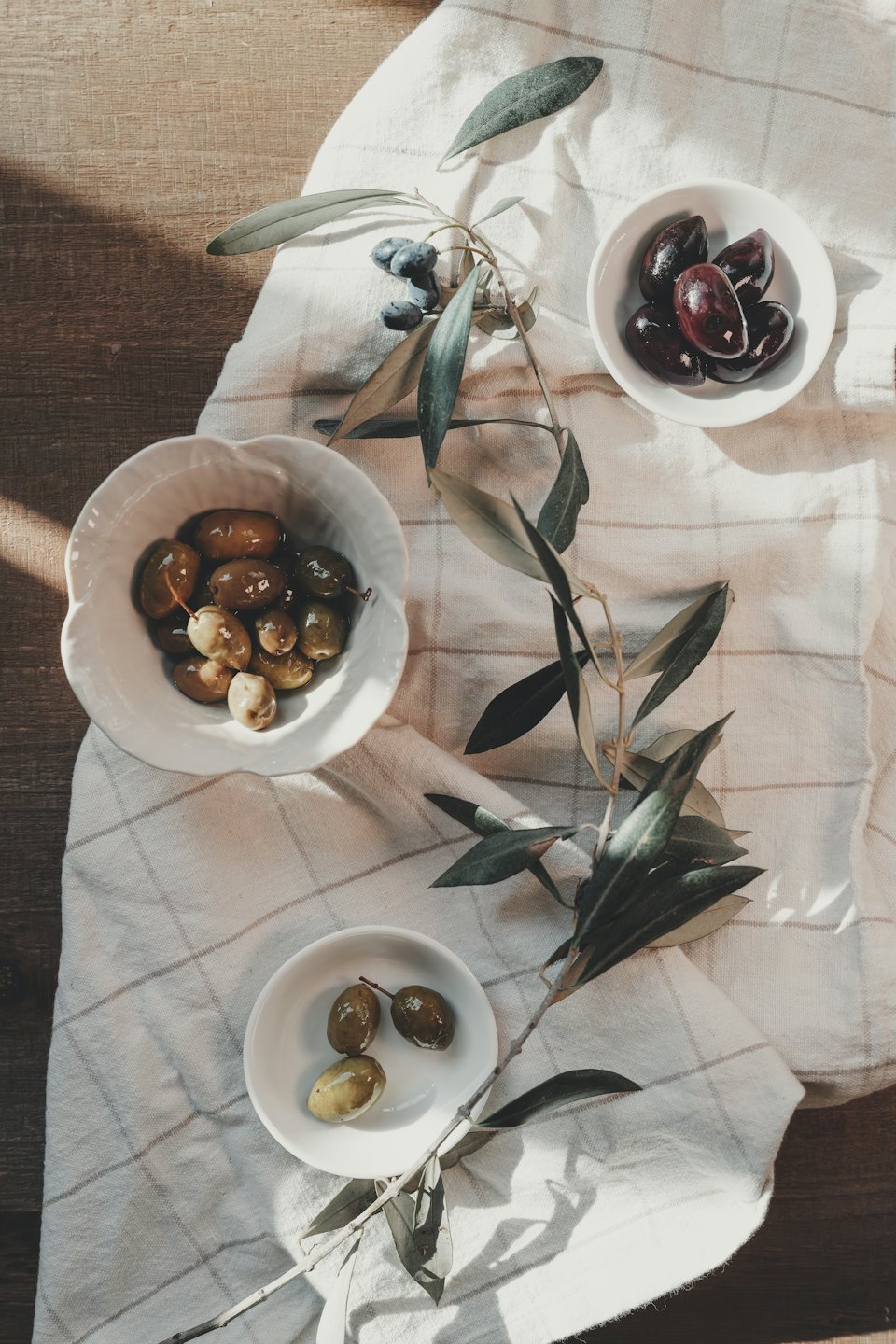 Tres cuencos de aceitunas variadas sobre una mesa de madera.