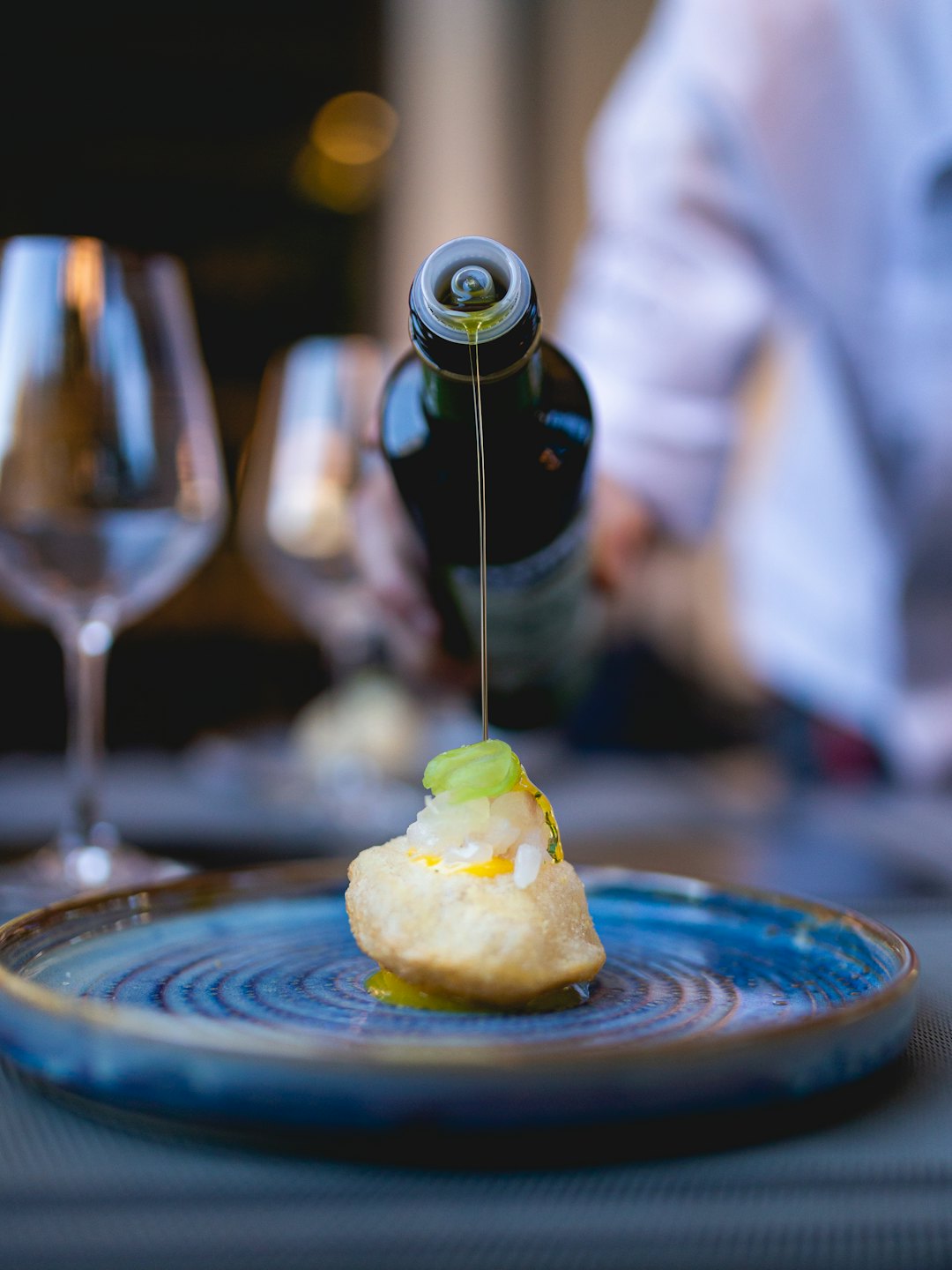 Chef vertiendo aceite de oliva sobre un aperitivo dorado.