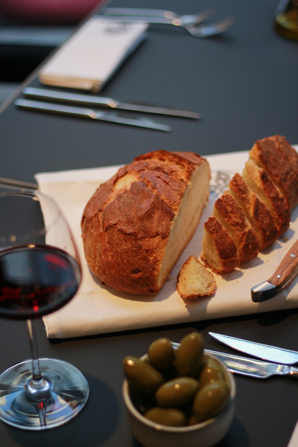 Pan artesanal, aceitunas y vino tinto en una mesa de restaurante.